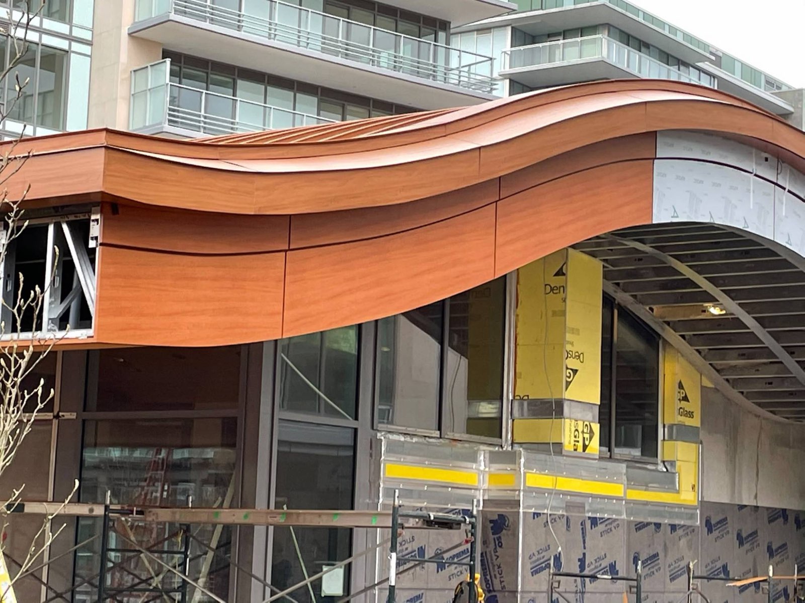 Curved wood-grain fascia sweeping over a glass storefront entrance