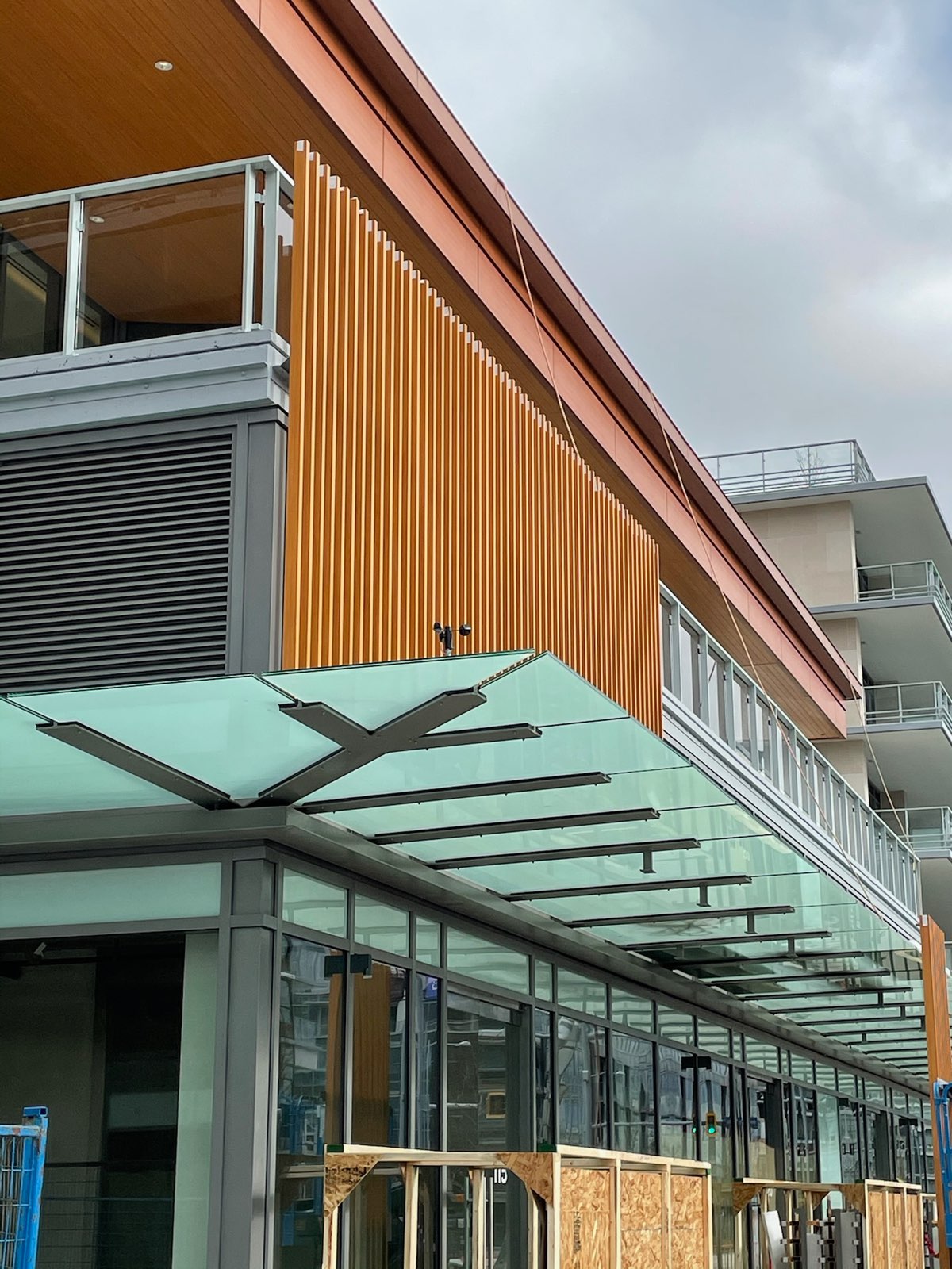 Frosted glass canopy below vertical wood-look louvers on a commercial building