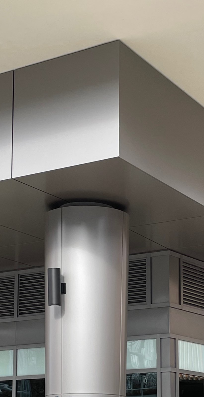 Round column and ceiling edge wrapped in brushed aluminum panels above a storefront