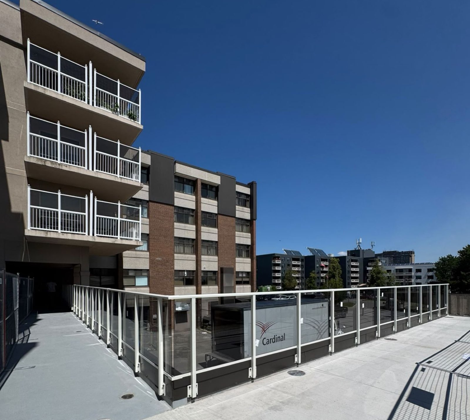 White railing with glass panels along a raised walkway beside a mid-rise building