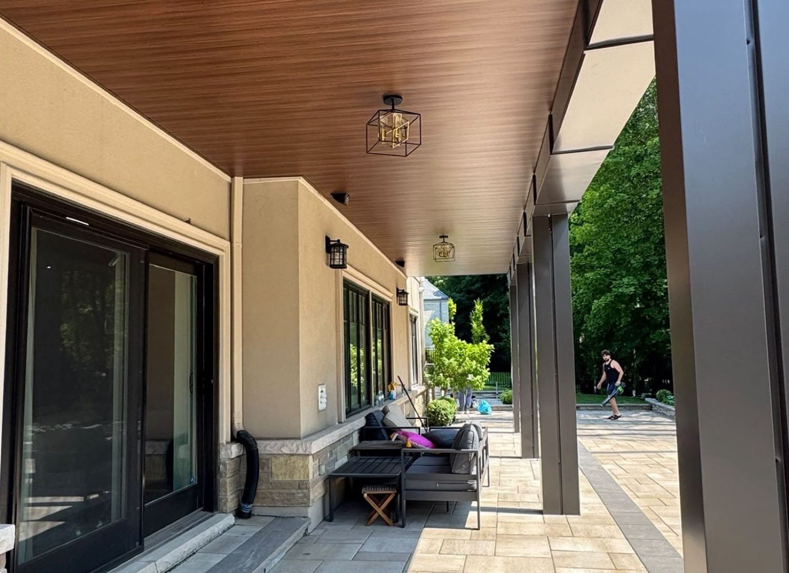 Wood-look soffit ceiling and dark columns over a covered patio beside a home