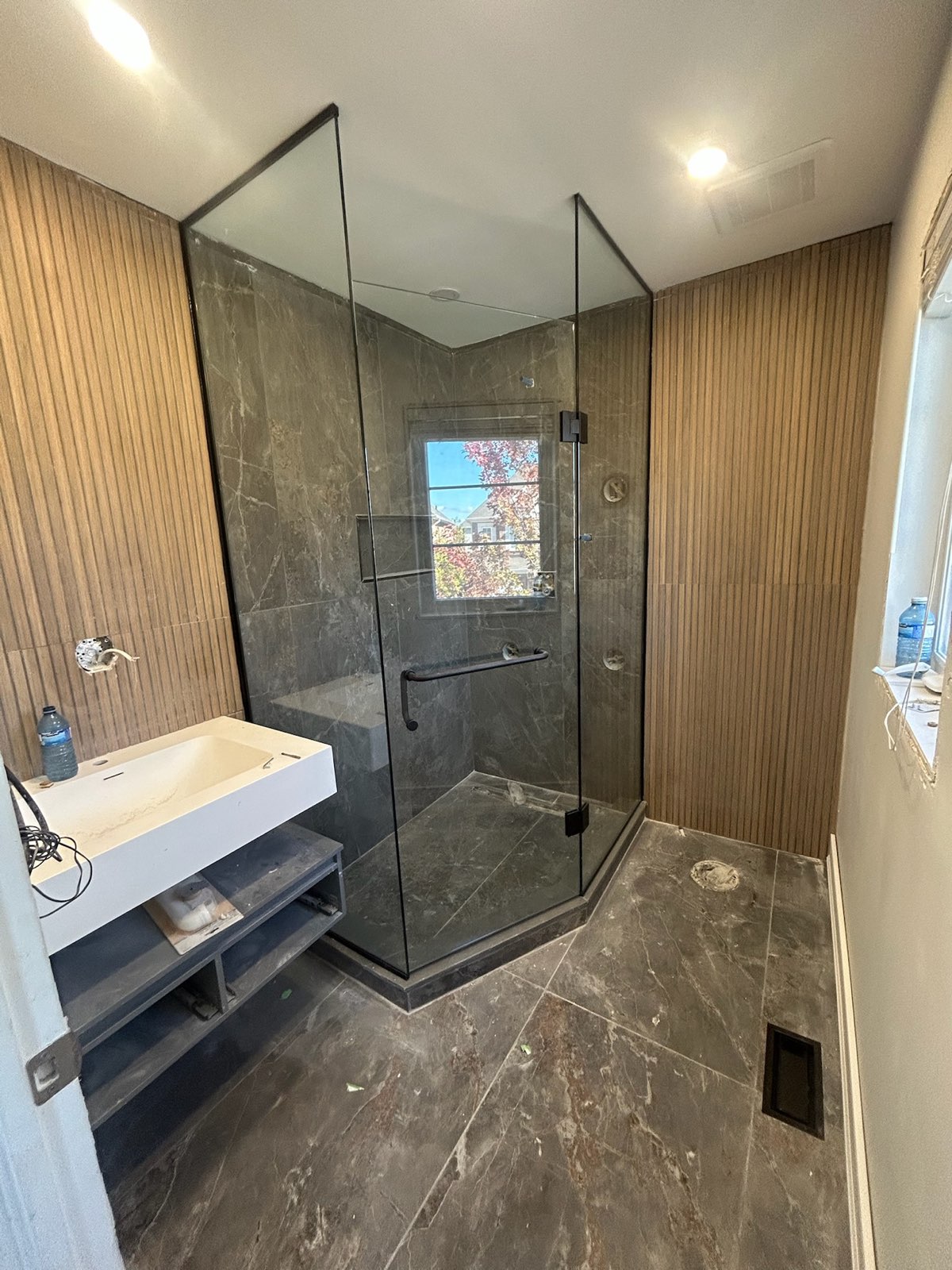 Frameless corner glass shower beside wood slat walls and a floating vanity