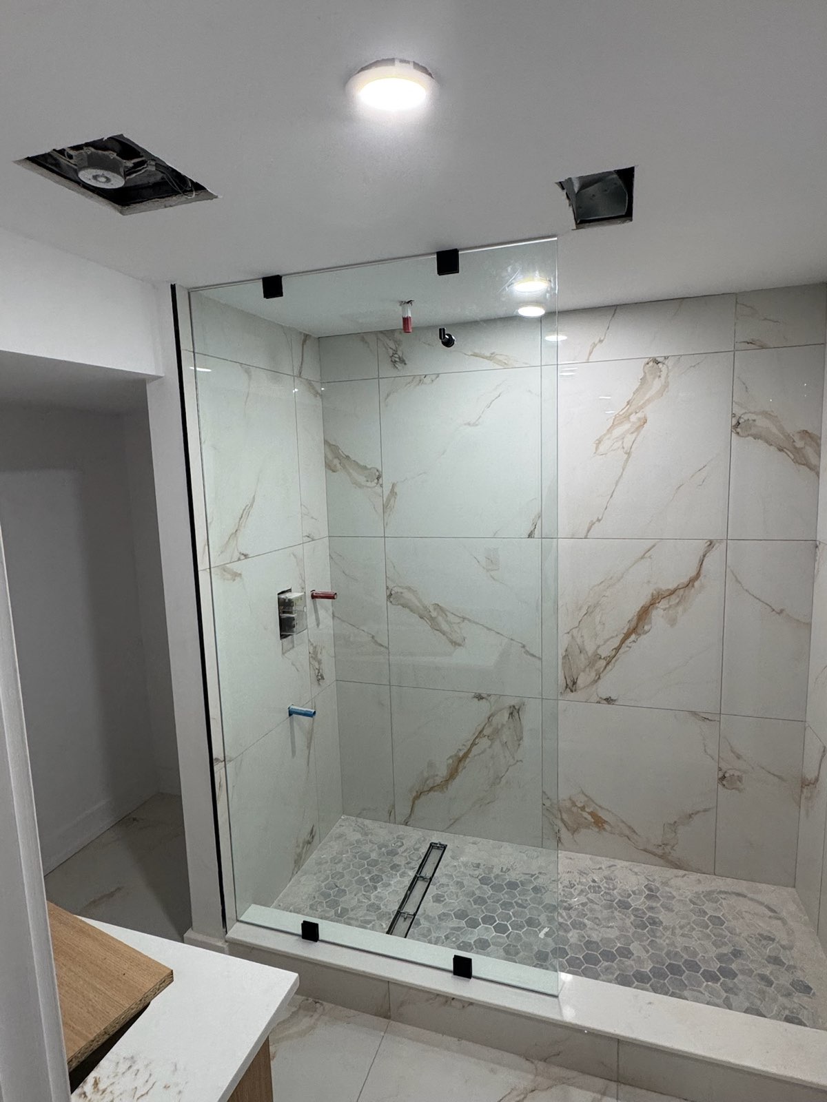 Frameless glass shower panel and door with black hardware on marble-look tile