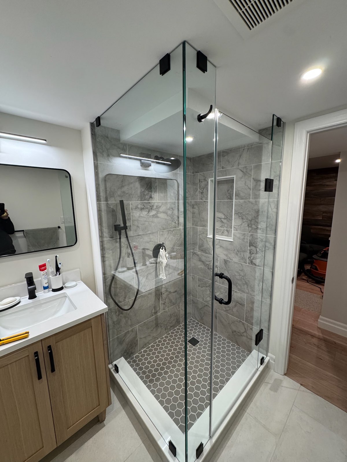 Frameless glass shower enclosure with a black handle next to a wood vanity