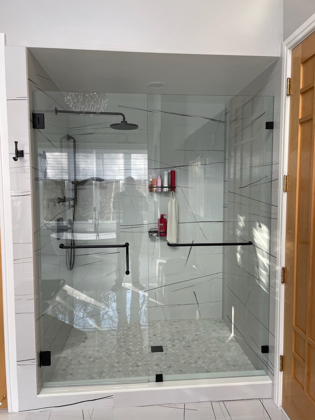 Frameless glass shower panel and door with black hardware in a white tiled bathroom