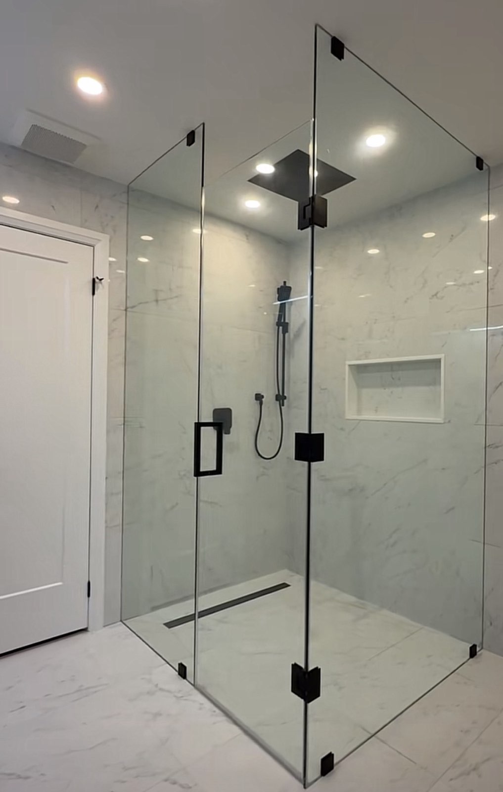 Corner frameless glass shower with black hardware in a white bathroom