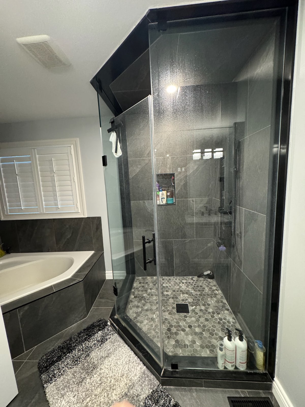 Neo-angle glass shower with black framing and a pebble-tile floor