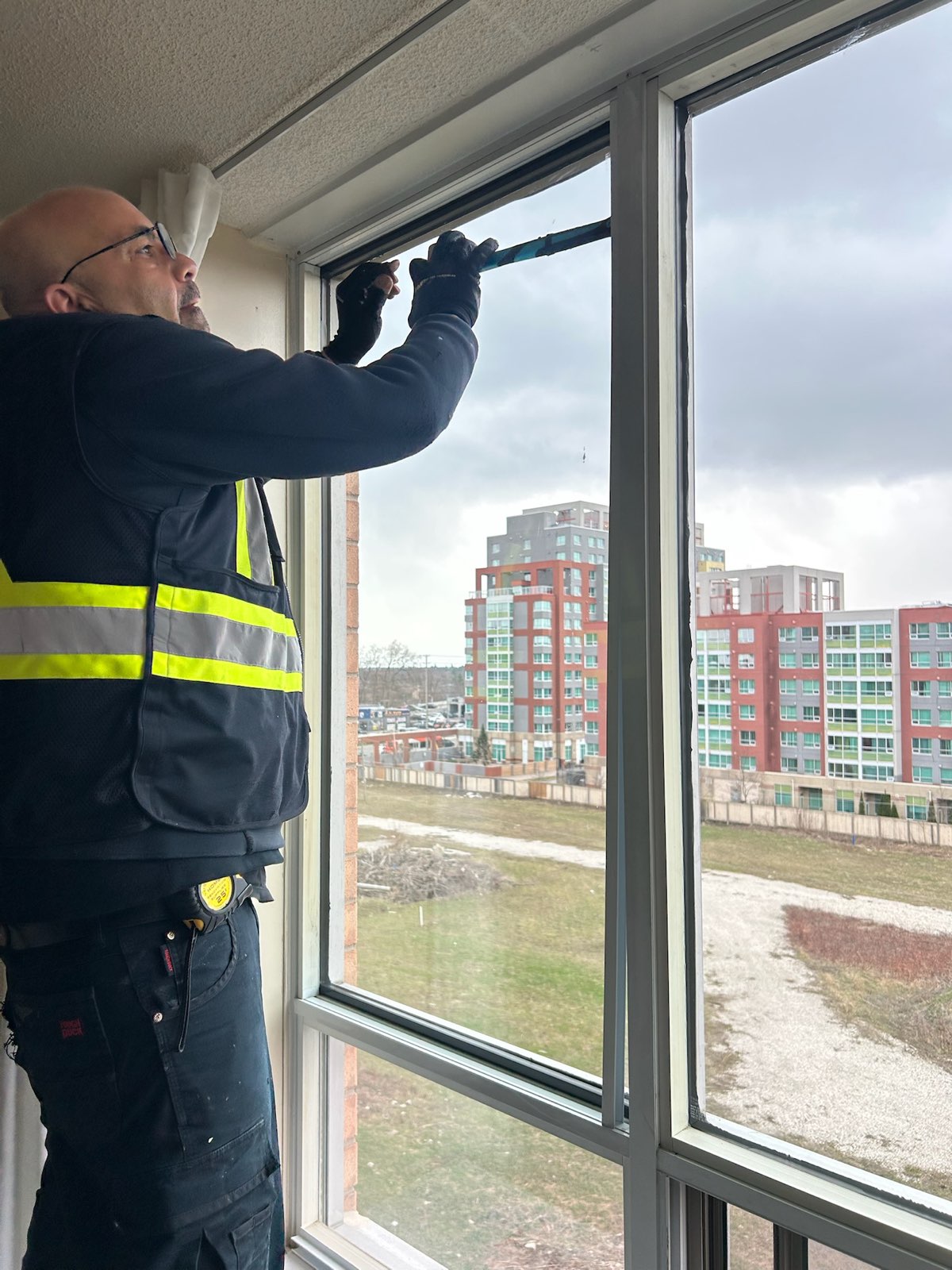Installer in a safety vest working on a high-rise window from inside the unit